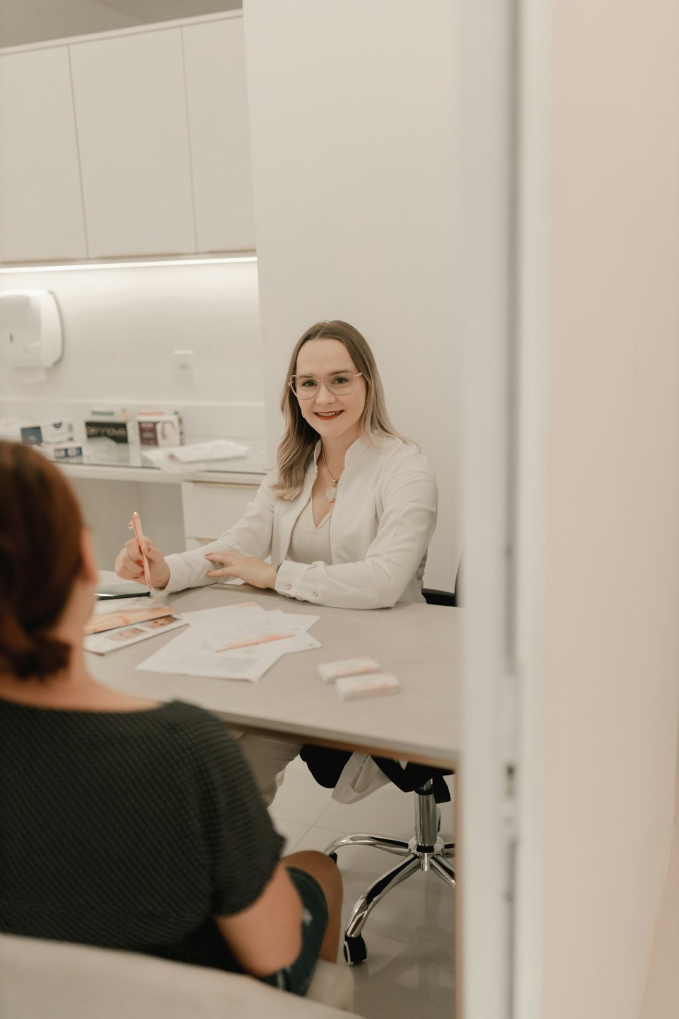 Femme en blouse de laboratoire souriant à un bureau avec un crayon.