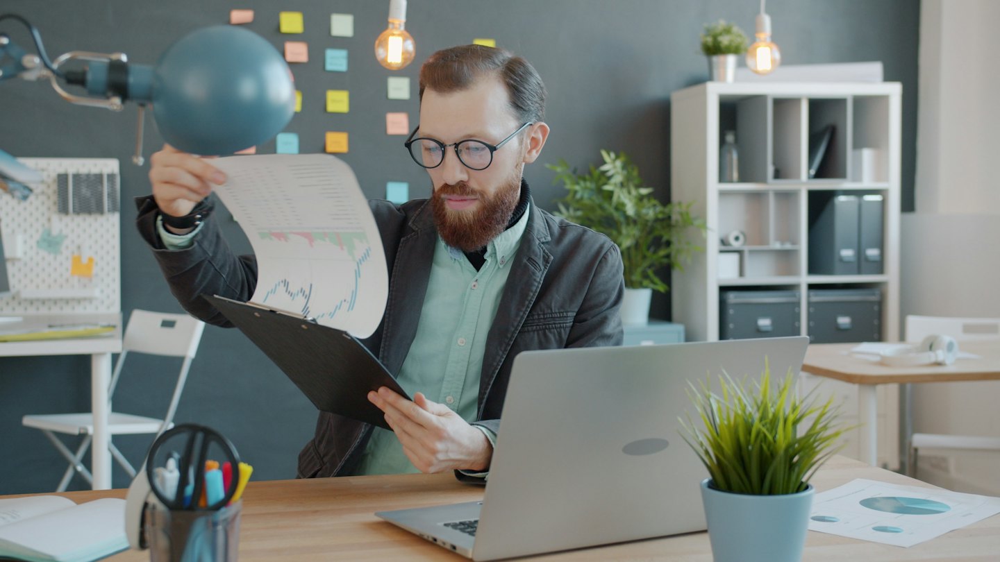 Un homme examine des graphiques financiers sur papier à son bureau en bois.