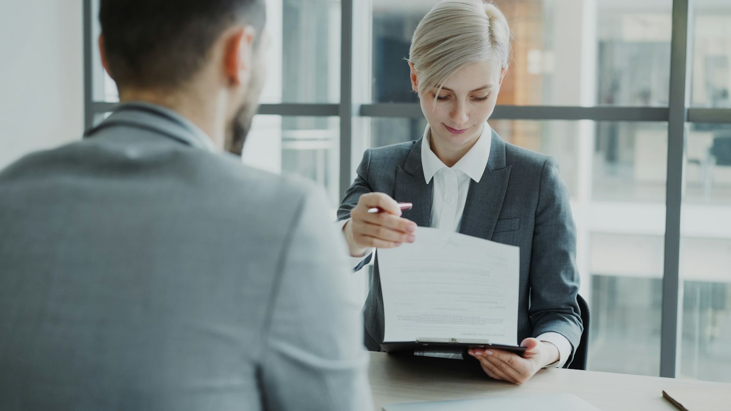 Une femme d'affaires tend un document et un stylo à un client dans un bureau.